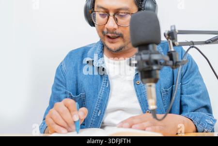 Man reading a book while recording a podcast or video in a studio with microphone, creating online content for his audience. Stock Photo