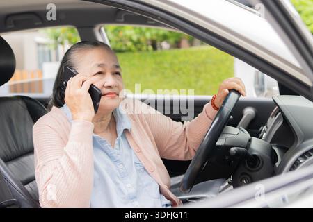 Elderly woman in a car, smiling, holding a smartphone. Senior woman using a phone, seated in a vehicle. Happy older lady with a mobile device in a car Stock Photo