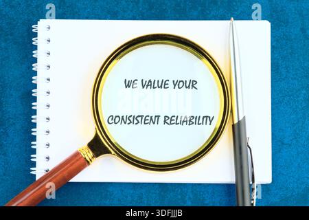 Magnifying glass focuses on message about value and reliability, situated on a white notepad with a pen on a blue background. Concept relates to busin Stock Photo