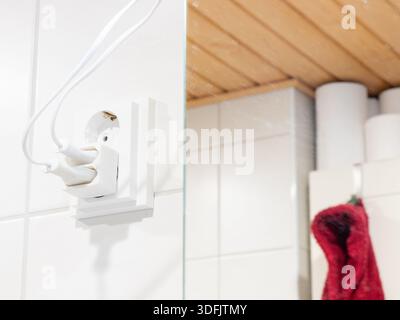 A white electrical outlet with an adapter has two cords plugged in against a tiled wall. The right side shows a mirror reflection of wooden ceiling, t Stock Photo