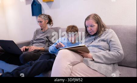 Family generations relaxing on a sofa, each using digital tablets and laptops Stock Photo