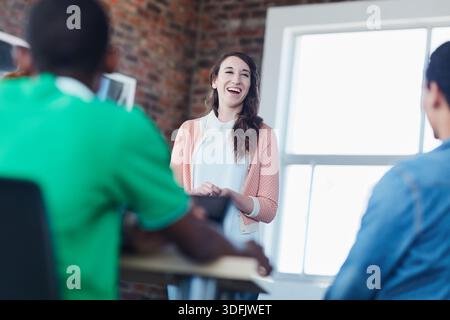 Lecturer, woman and laugh with students at college for funny lesson, exam preparation and learning. Education, female tutor or happy with people in Stock Photo