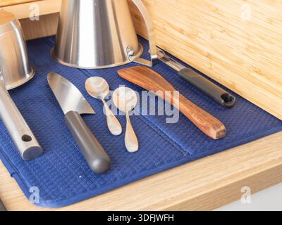 A kitchen drawer organizes various metal utensils on a blue mat, suggesting domestic efficiency, culinary preparation, and tidy home storage for cooki Stock Photo