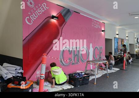 Two men hand paint a Vodka Cruiser street advertisement mural on a city wall in Brisbane City, Queensland, Australia, January 2026. Stock Photo