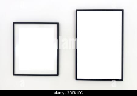 Two empty black photo frames of different sizes hanging on a white wall. Minimalist mockup for poster, artwork, or photography presentation. Stock Photo