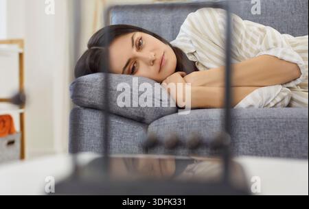 Frustrated young woman looking at Newton's cradle balance balls lying on sofa at home Stock Photo