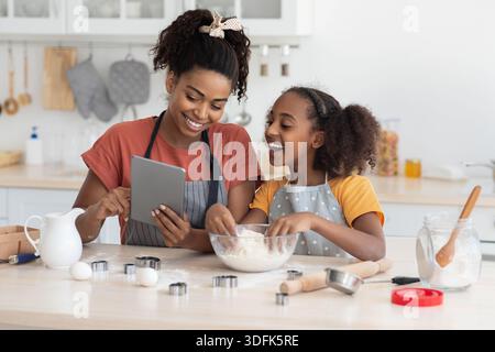 Black mummy and daughter cooking at home, using tablet Stock Photo