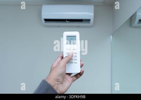 A hand holds an air conditioner remote control, setting the temperature to 25°C for energy efficient level. Climate control, home comfort, and energy Stock Photo