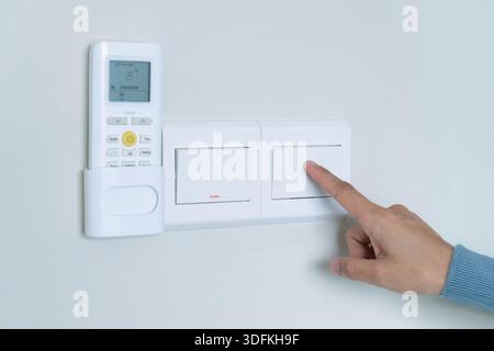 A person's hand turning off a light switch. Conserve electricity, energy saving and practice energy efficiency at home concept. Stock Photo