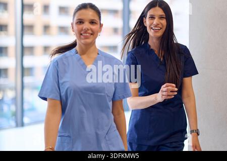 Two healthcare professionals walk together in a modern hospital setting during daytime Stock Photo