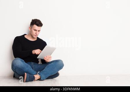 Young Man Sitting on Floor Using Tablet in a Minimalistic Room Setting Stock Photo