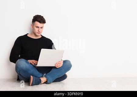 Young Man Sitting on Floor Using Laptop in Modern Indoor Setting Stock Photo