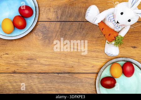 Six colourful Easter eggs on two plates in pastel colours and Easter bunny holding carrot on vintage reclaimed oak background, top view Stock Photo