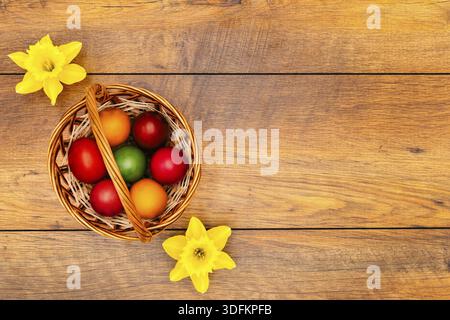 Seven colourful Easter eggs in pastel colours in the basket and two yellow daffodils on vintage reclaimed oak background, top view Stock Photo