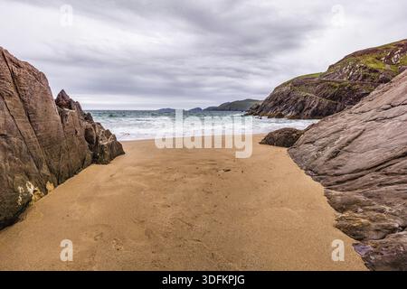 View from small hidden beach between rocks towards cliffs and islands in the distance, moody stormy clouds Stock Photo