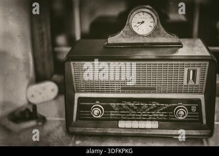Old vintage radio receiver of the last century with rustic clock on top on window sill, front view, sepia style Stock Photo