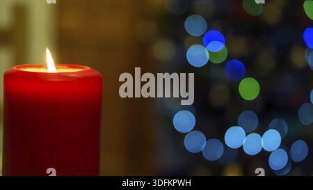 One large red burning candle on abstract blurred background with big circular colourful bokeh Stock Photo