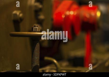 Selective focus on large vintage valve wheel and thread with blurred red and coper pipes and tanks in background Stock Photo