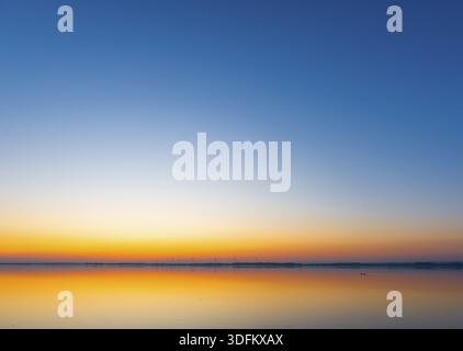 A calm sunrise with a soft color gradient is reflected in the still water of Lake Dduemmer, Duemmer nature park Park, Lower Saxony, Germany Stock Photo