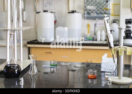 Pipette and colourful chemical liquid solutions in flasks on laboratory worktop, lab equipment and glassware in background Stock Photo