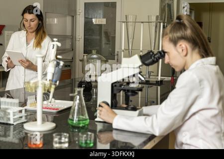 Team of two, Caucasian white, female laboratory technicians in white robes working in chemical or pharmaceutical laboratory, laboratory equipment and Stock Photo