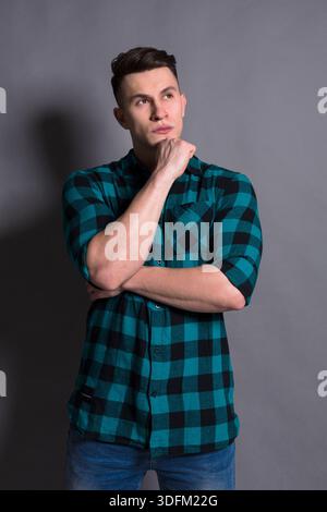 Young Man in Checkered Shirt Thoughtfully Poses Against a Gray Background Stock Photo