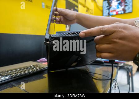 MSI gaming laptop being held by a person pointing to a broken section near the rear fan exhaust, in a computer repair shop. Cebu, Philippines Stock Photo