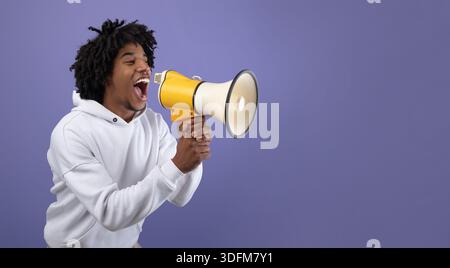 Emotional black teen guy shouting into megaphone, announcing breaking news over violet background Stock Photo