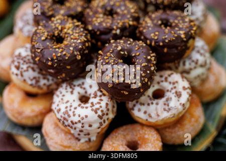 A close-up view of stacked mini donuts covered with chocolate, white glaze, and sprinkled toppings. The image highlights texture and color in a desser Stock Photo