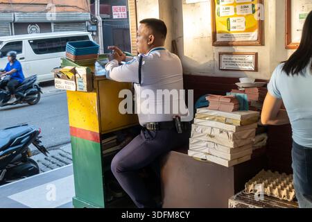 security guard at entrance booth, pawnshop in Cebu, Philippines.  The guard is in uniform, seated at a small, colorful counter. Stock Photo