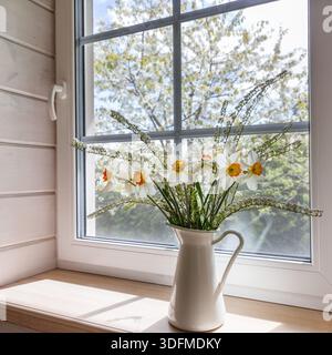 Spring daffodils in white jug on wooden windowsill, cozy cabin interior Stock Photo