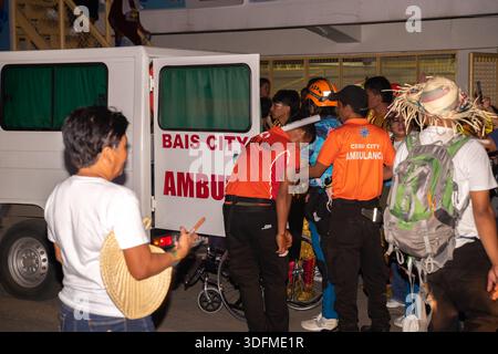 Emergency response, an ambulance from Bais City, Philippines, and personnel in orange shirts, one of whom has a "Cebu City Ambu" patch Stock Photo