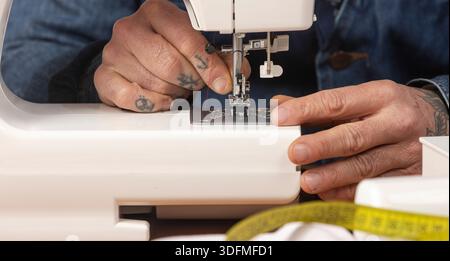 Craftsperson's tattooed hands preparing a domestic sewing machine with red thread for textile work Stock Photo