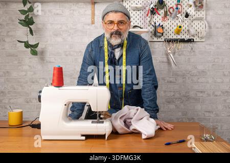 Male fashion designer working in his workshop with a sewing machine and fabric Stock Photo