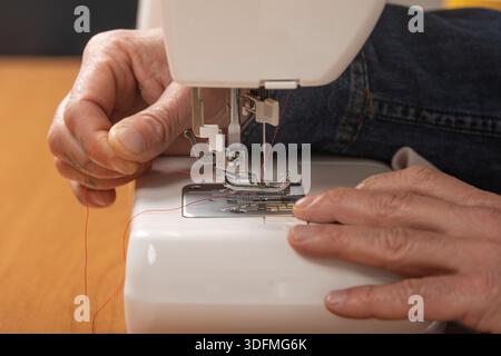 Hands threading red yarn into a sewing machine, preparing for sewing Stock Photo