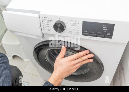 Man putting dirty clothes in washing machine drum, lifestyle household chores Stock Photo