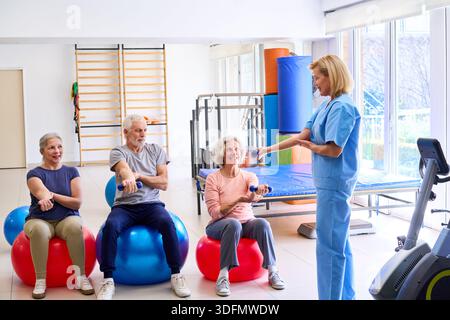 Senior adults are doing arm exercises with dumbbells on exercise balls with a physiotherapist in a rehab center. This image can be used for recovery a Stock Photo