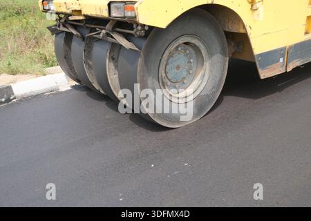 Road roller compacting fresh asphalt during road construction, close-up of heavy machinery, pneumatic compactor, on newly paved street. Stock Photo