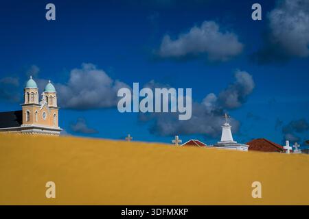 View of golden light casting over the rooftops and church spires against a vibrant blue sky dotted with fluffy white clouds, Willemstad, Curaçao. Stock Photo