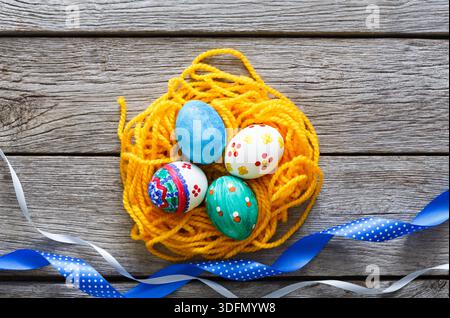 Colorful Easter Eggs Arranged in a Nest of Yellow Yarn With Decorative Ribbons Nearby Stock Photo