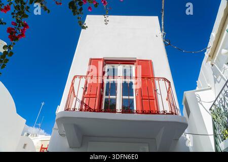 View of bright red shutters and balcony contrasting against the stark white building facade under a vibrant blue sky, Old town, Mykonos, Greece. Stock Photo