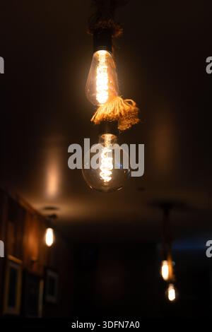 Two Edison-style filament light bulbs hang from ropes, illuminating a dark room with a warm glow. Stock Photo