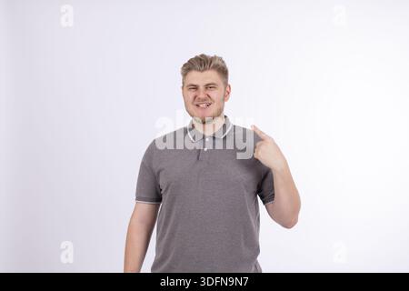 Man pointing at himself with thumbs with proud facial expression on white wall Stock Photo