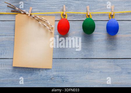 Colorful Decorative Eggs Hang on a String Next to a Blank Note on Wooden Background Stock Photo