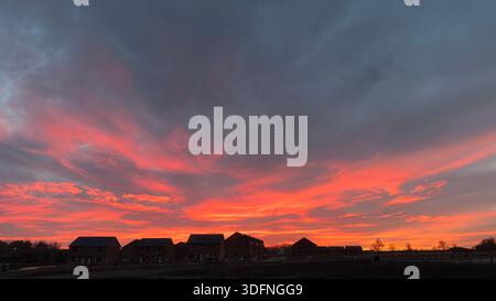 A dramatic sunset paints the sky in vibrant oranges and reds, silhouetting a line of houses against the horizon. Stock Photo