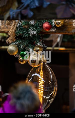 A large Edison bulb hangs amidst festive Christmas decorations, with pine branches, baubles, and a rustic wooden beam. Stock Photo