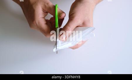 Man cuts a snowflake out of a paper napkin with scissors. Making paper crafts. Fine motor skills. Hand training and concentration. Christmas Stock Photo