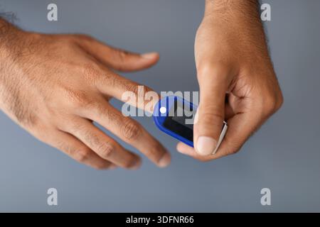 Unrecognizable man using pulse oximeter, grey background Stock Photo