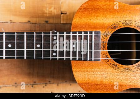 A classic brown acoustic ukulele with white wooden strings rests on a rustic wooden table like a folk musical instrument ready to play a jazz and rock Stock Photo