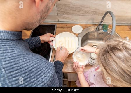 Family man and girl cook pancakes in kitchen, father and daughter spend time together Stock Photo